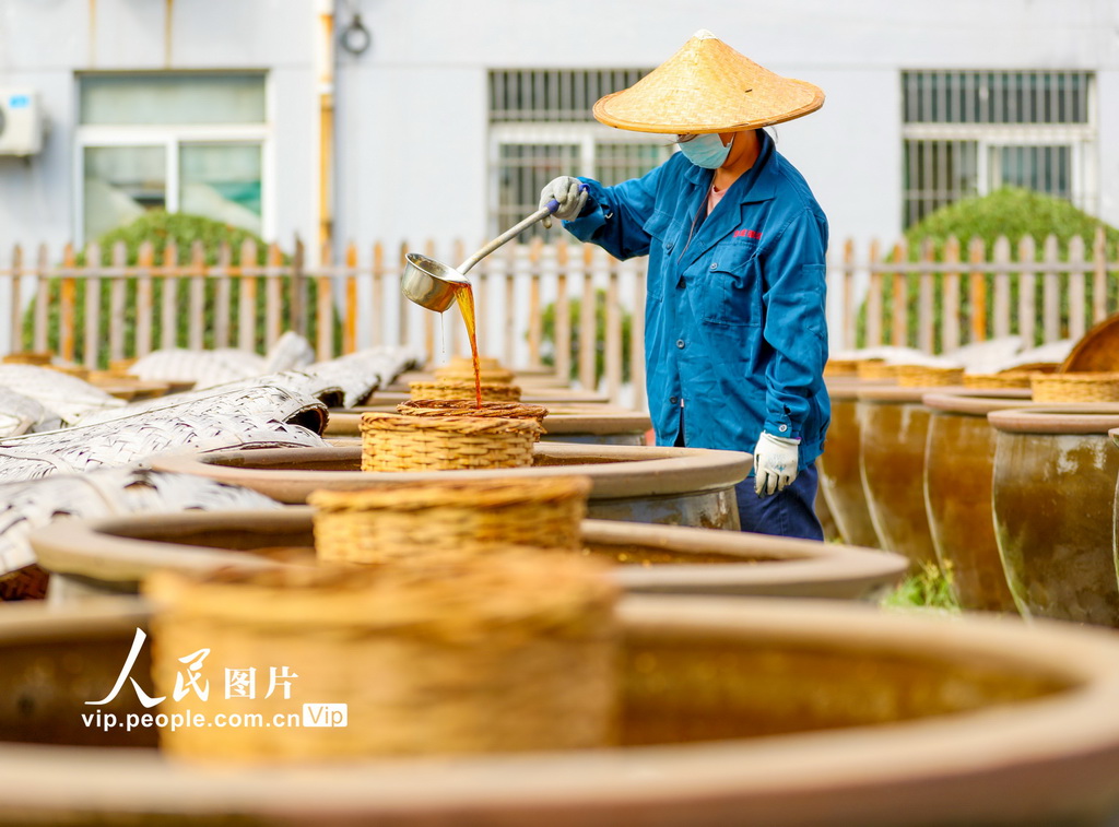 2024年9月21日，山东滕州市一家酱醋食品有限公司的工人在晾晒场上浇淋晒制酱油。