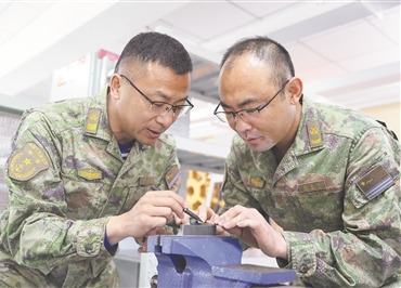一级军士长赵三雷（左）与张庆山探讨钳工工艺。